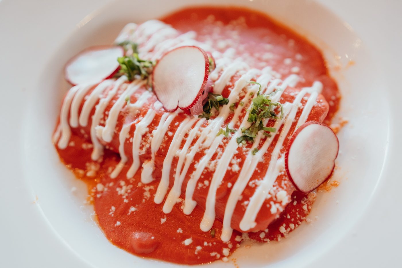 Enchiladas de la Casa covered in red salsa, crema, queso fresco, and radish