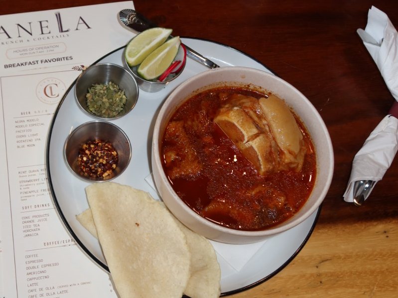 A bowl of Menudo served with lime, oregano, chili flakes, and warm corn tortillas